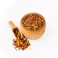 Wooden bowl and scoop full of crushed red cayenne pepper, a dried chili flakes and seeds isolated on white background. Homemade spices ingredients for cooking.