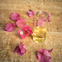 Obraz na płótnie Canvas Close-up of essential oil in a small glass bottle with bougainvillea flowers on wooden background. Selective focus and copy space for text. Portrait format