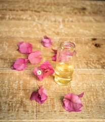 Obraz na płótnie Canvas Close-up of essential oil in a small glass bottle with bougainvillea flowers on wooden background. Selective focus and copy space for text. Portrait format
