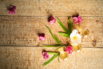 Essential oil in small glass bottles with bamboo leaves, bougainvillea and frangipani flowers on wooden background. Selective focus. top view and copy space for text. Natural cosmetics.

