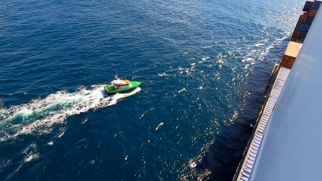 Pilot boat approach to the cargo container ship. Pilot disembark by pilot ladder.
