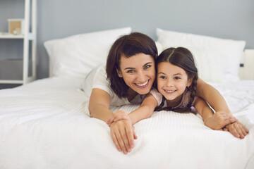 Happy mother and daughter lying together on bed and looking at camera