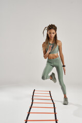 Workout. Full length shot of young sporty mixed race woman in sportswear training on agility ladder...