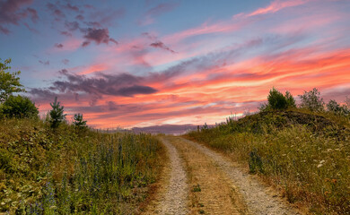 Fototapeta na wymiar A path with trees on the side of a hill under a colorful dramatic sunset sky. High quality photo