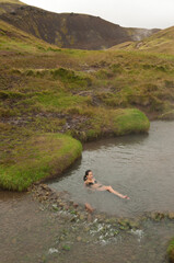Girl bathing in Icelandic geothermal hot spring during surrounded by mountains in a cold summer day in Iceland