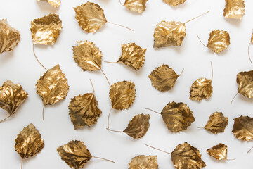 Pattern made with autumn dry leaves colored with golden paint arranged randomly on white background.