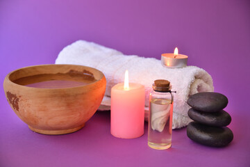 Obraz na płótnie Canvas Spa and beauty salon background scene with a towel, wooden bowl, candle, and stone isolated on a purple background. Wellness and health care concept. Close up, selective focus