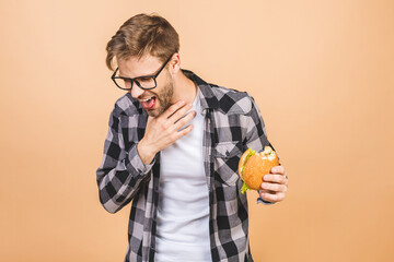 Handsome young man refusing unhealthy burger isolated over beige background. Diet concept. With...