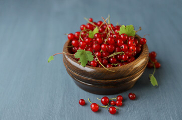 Red ripe black currant berries in a wooden bowl on a gray background. Selective focus. The harvest of berries.