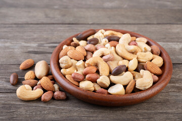 A wooden plate full of mixed nuts over a wooden background. Peanuts, brazilian nuts, cashew nuts, baru nuts and almonds