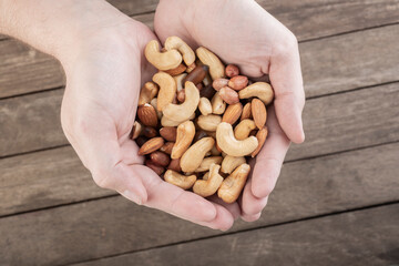 Hands full of mixed nuts over a wooden background. Peanuts, brazilian nuts, cashew nuts, baru nuts and almonds