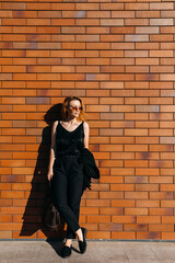 Fototapeta na wymiar Young confident woman, wearing black suit, standing on a brick wall background on the street.