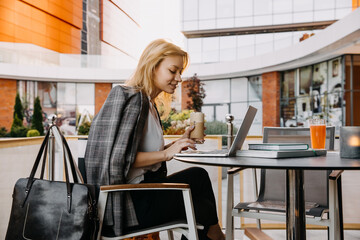 Young modern woman working on laptop at a cafe terrace. Business and office free concept.