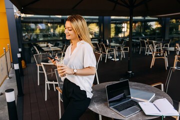 Young stylish woman holding a smartphone and a glass of ice coffee at a cafe terrace. Coffee break concept.