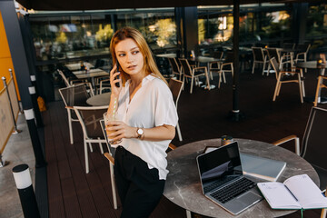 Young modern woman talking on the phone at a cafe terrace. Business concept.
