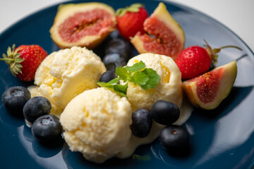 three scoops of ice cream, figs, blueberries, and a mint leaf on a blue plate