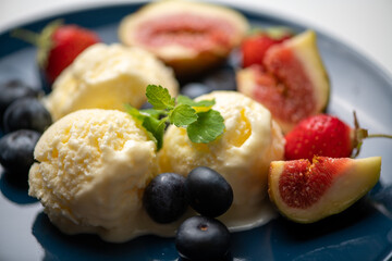 three scoops of ice cream, figs, blueberries, and a mint leaf on a blue plate