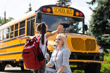 Mother brings her daughter to school near the school bus. back to school