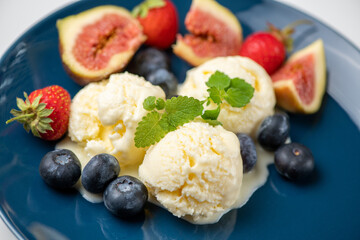 three scoops of ice cream, figs, blueberries, and a mint leaf on a blue plate