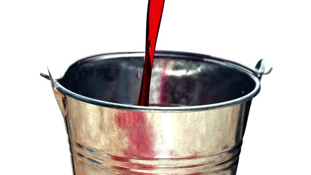 The red liquid is poured into a steel bucket until to edge, isolated on white background, slow motion.