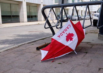 Broken discarded umbrella on sidewalk, featuring the Canadian flag maple leaf