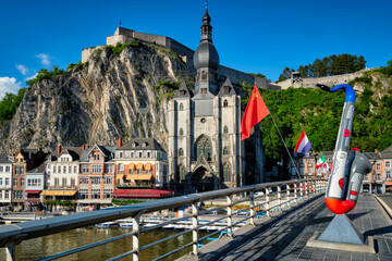 Picturesque Dinant town, Dinant Citadel and Collegiate Church of Notre Dame de Dinant and Charles de Gaulle bridge with saxophones as Dinant is hometown of saxophone inventor and flags. Namur, Blegium - obrazy, fototapety, plakaty