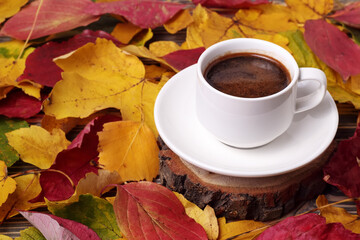 White cup of coffee and autumn yellow leaves around on wooden table in the fall.