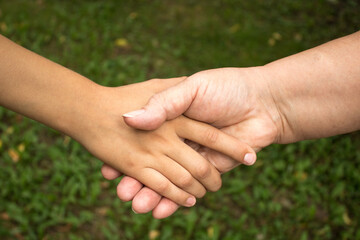 A grandmother and a child shake hands against a background of green grass. The concept of love and friendship between generations. International Day of Older Persons and Grandparents Day.