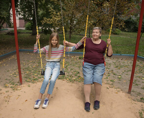 Grandmother and granddaughter ride on a swing in the yard. The concept of love and friendship  between generations. International Day of Older Persons and Grandparents Day