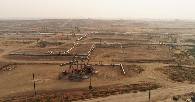 Pump jack in vast oil fields in California. Pipelines transporting oil from oil pumps, aerial drone shot