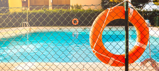 View of a salt water pool from the fence with a orange life float on a sunny summer day.