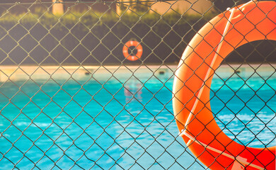 View of a salt water pool from the fence with a orange life float on a sunny summer day.