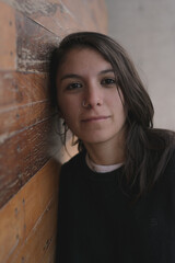 Joven mujer mirando hacia adelante apoyada en pared de madera 