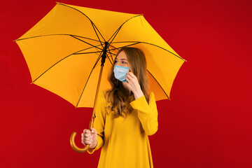 young woman in a dress and a medical protective mask on her face, with an umbrella in her hands, on a red background