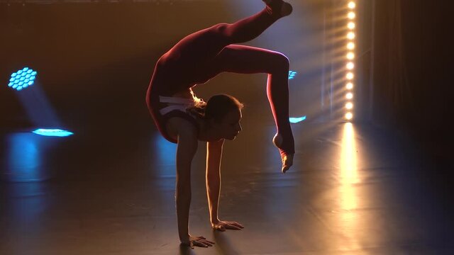 A girl gymnast in a tight sports bodysuit performs gymnastics elements and demonstrates a wonderful stretch. Silhouette. Slow motion. Close up.