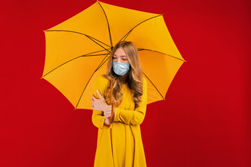young woman in a medical protective mask on her face, with an umbrella in her hands on a red background