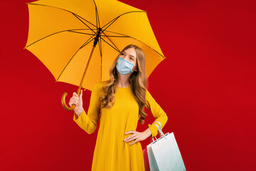 Happy young woman in a medical mask, with shopping bags and umbrella, on a red background