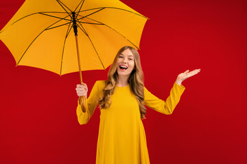Shocked happy young woman, with a yellow umbrella on a red background
