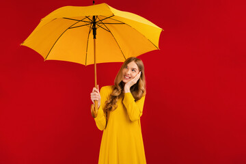 Happy thoughtful young woman with a yellow umbrella on a red background