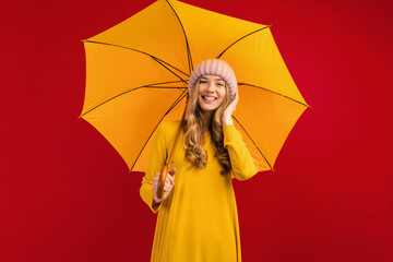 Happy beautiful young woman with an umbrella in a warm hat on her head, on a red background