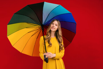 Happy young woman with a rainbow umbrella, on a red background
