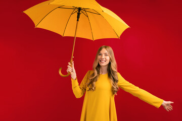 Beautiful happy young woman with yellow umbrella on red background, autumn concept