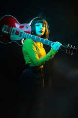 Hipster woman with curly hair with red guitar in neon lights. Rock musician with electrical guitar....