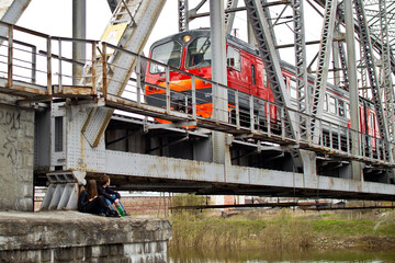A guy and a girl are sitting under the bridge while the train is moving