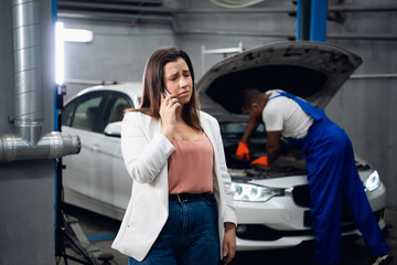 A customer is talking on the phone. Workshop worker in the background repairing a car