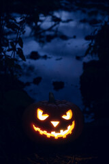 Glowing Halloween pumpkin in the forest at night. Vertical orientation, copy space.