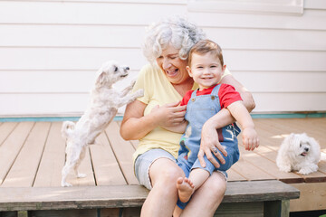Grandmother sitting with grandson boy on porch at home backyard. Bonding of relatives and generation communication. Old woman with baby having fun spending time together outdoors.