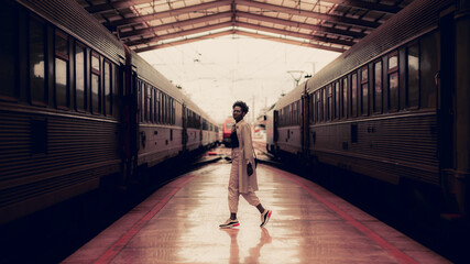 A dark pinkish interior of a railway station depot with charming elegant black tourist girl in...