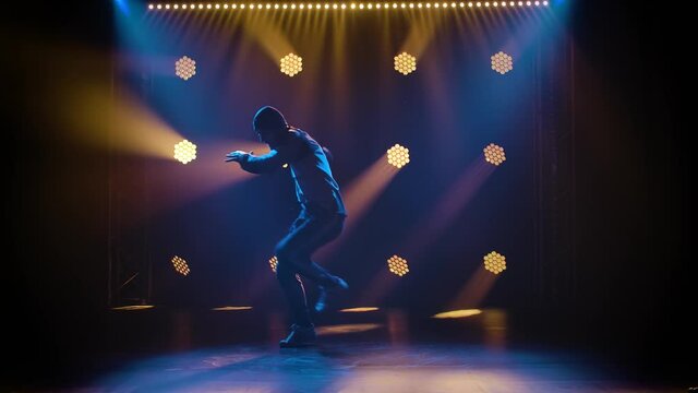 Handsome young man dancing break dance, hip hop, street dancing in studio, isolated. Shot in the studio against a black background with dynamic neon lights. Silhouette. Slow motion.