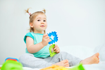 Child holds detail from multicolored constructor while sitting on bed